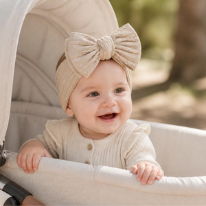 Smiling baby in an oat soft bow headband sitting in a pram