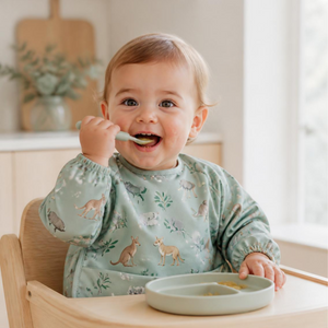 Baby in a sage animal print smock bib being spoon fed
