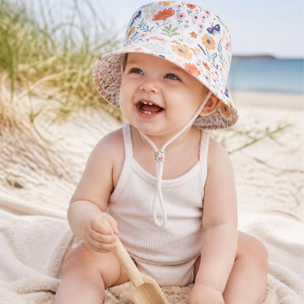 Laughing baby in a floral bucket sun hat at the beach