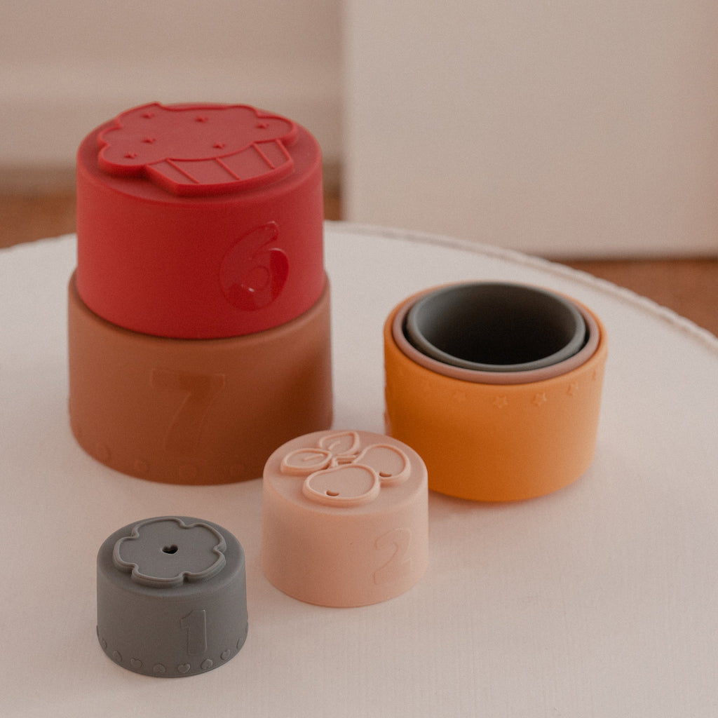 Silicone Baby Stacking Cups Bath & Beach in Earthy — baby hat styled flat lay with nursery accessories