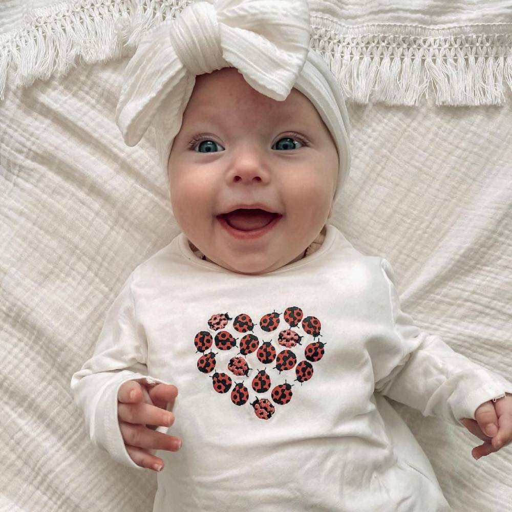 Bowie Double Bow Baby Headband in White — baby headband styled flat lay with nursery accessories