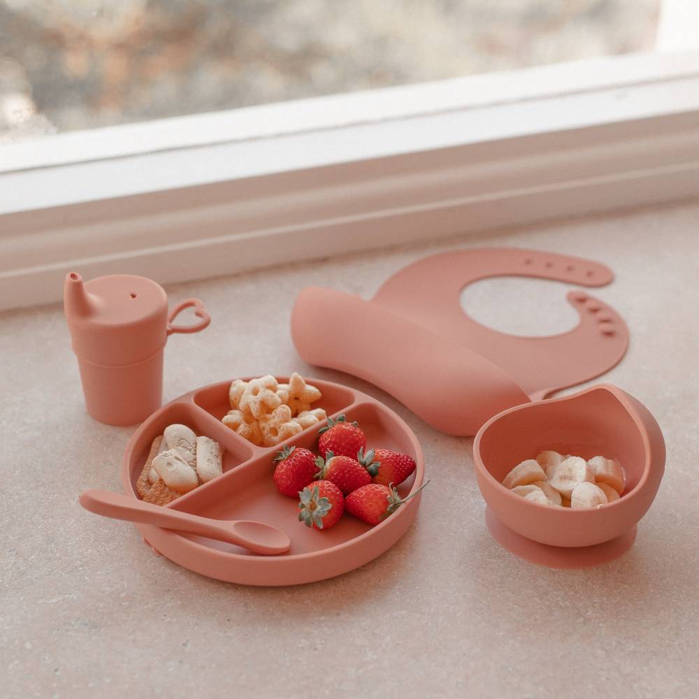 Baby wearing brandy rose baby bib during mealtime — Silicone Baby Feeding Set