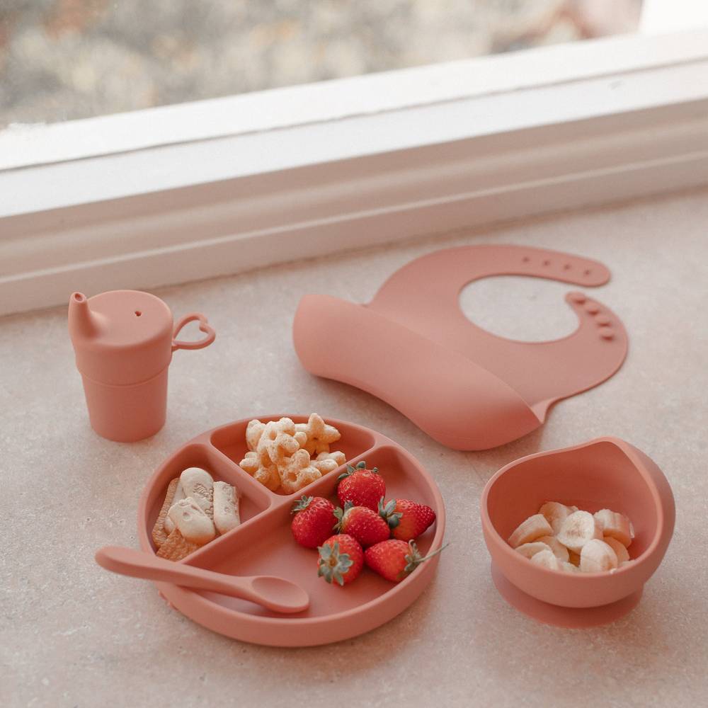 Baby wearing brandy rose baby bib during mealtime — Silicone Baby Feeding Set