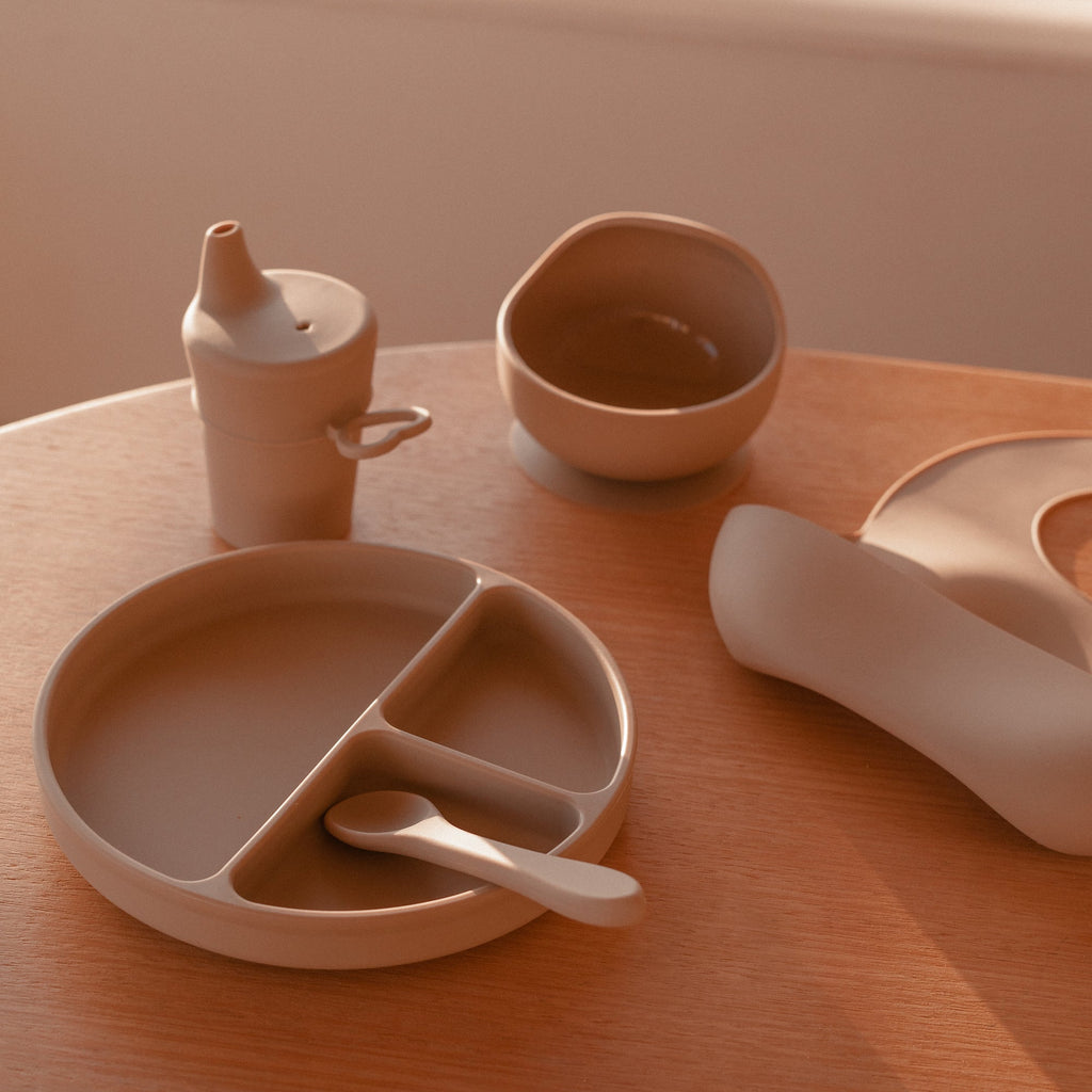 Silicone Baby Feeding Set in Sand Dune — baby bib styled flat lay with nursery accessories