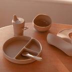 Silicone Baby Feeding Set in Sand Dune — baby bib styled flat lay with nursery accessories