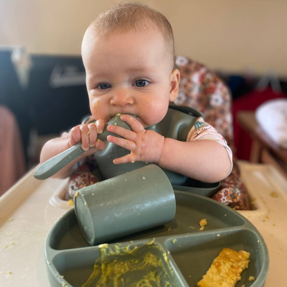 Silicone Baby Feeding Set in Chalet Green — baby bib styled flat lay with nursery accessories
